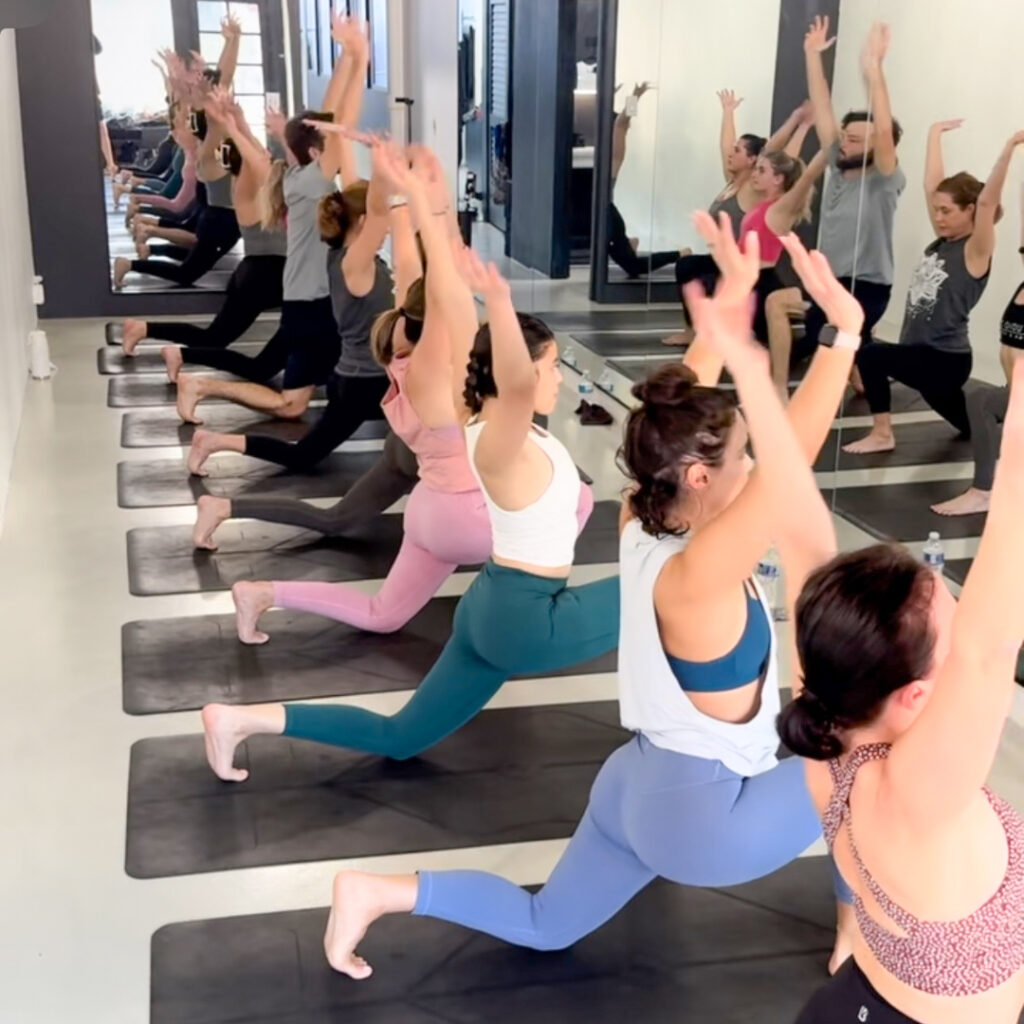 Seven yogis are seen in a lunge pose during Inside Flow class at Studio 311 Yoga Daytona Beach, FL.