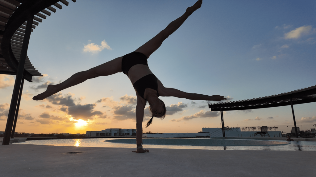 Sherri Meyers is demonstrating a one arm handstand and split by the pool in Tulum Mexico