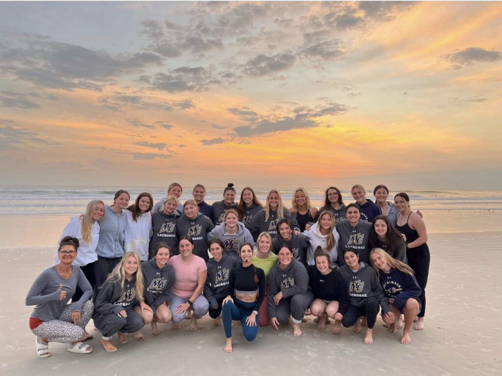 Group photo of the  Merrimack College Women's Lacrosse Team (2023) after their sunrise yoga on the beach session with Sherri Meyers.