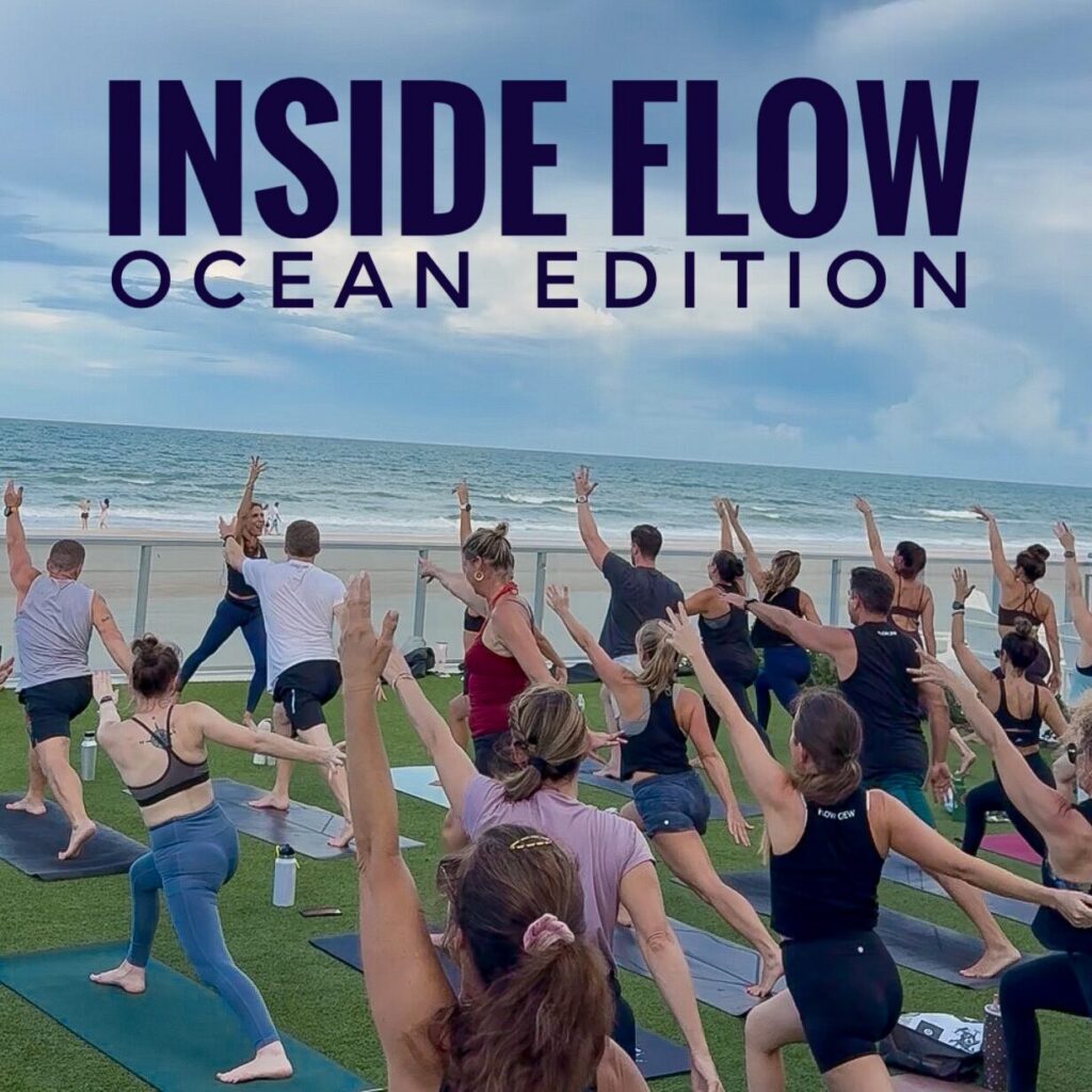 “Inside Flow: Ocean Edition” yoga class on a beachside deck at Renaissance Daytona Beach, FL, with a group stretching on mats beside the sea under a cloudy sky; energetic, communal mood. The Inside Flow yoga class is taught by Sherri Meyers of Studio 311 Yoga.